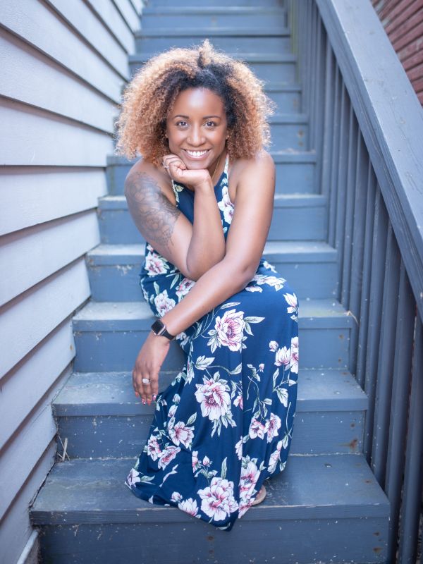 image of Charla, Black woman with curly hair siting on blue stairs in a dress